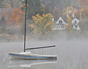 Foggy Fall morning on calm lake with boat Maine